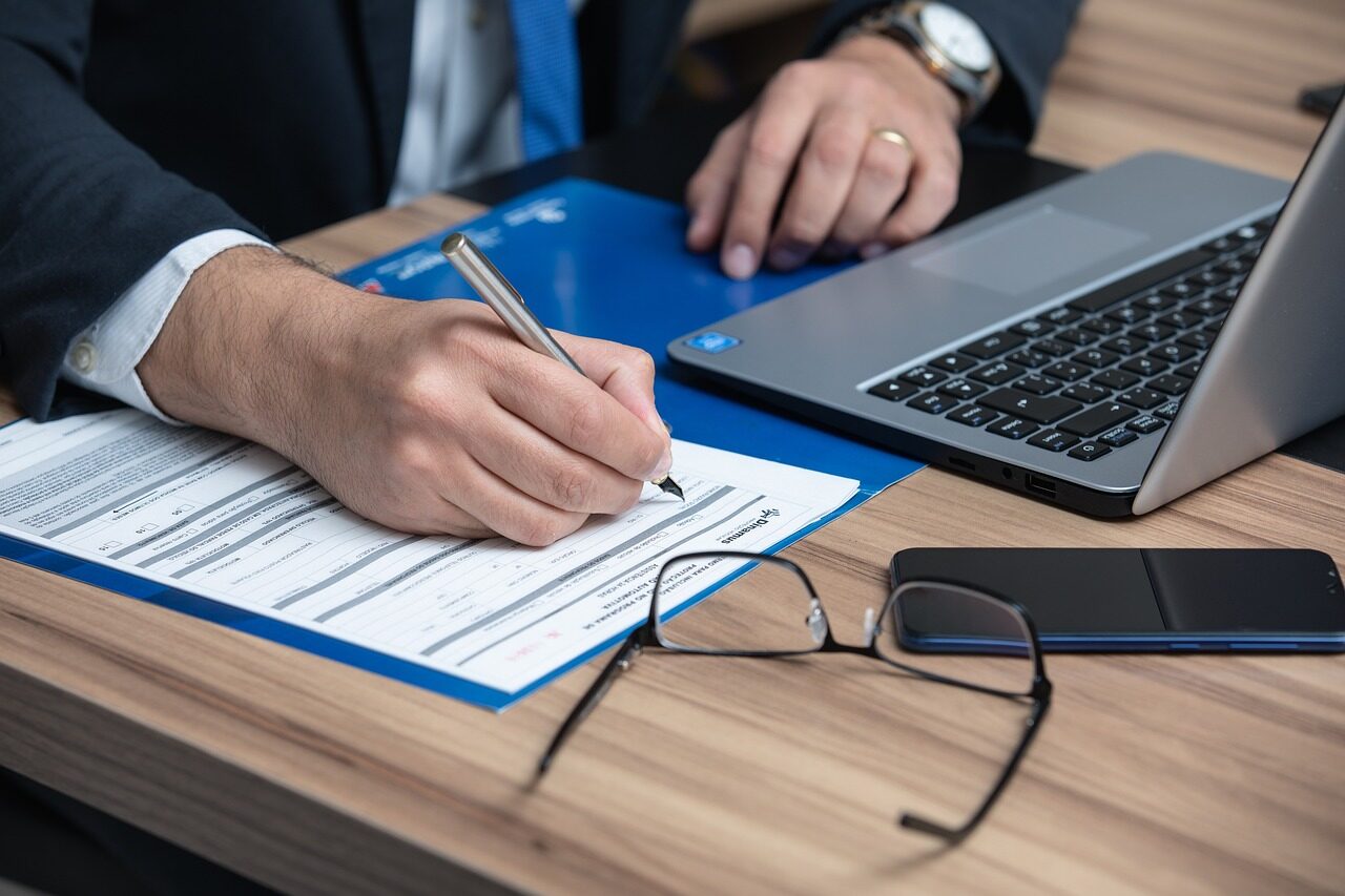 Persona firmando un contrato junto a un ordenador portátil